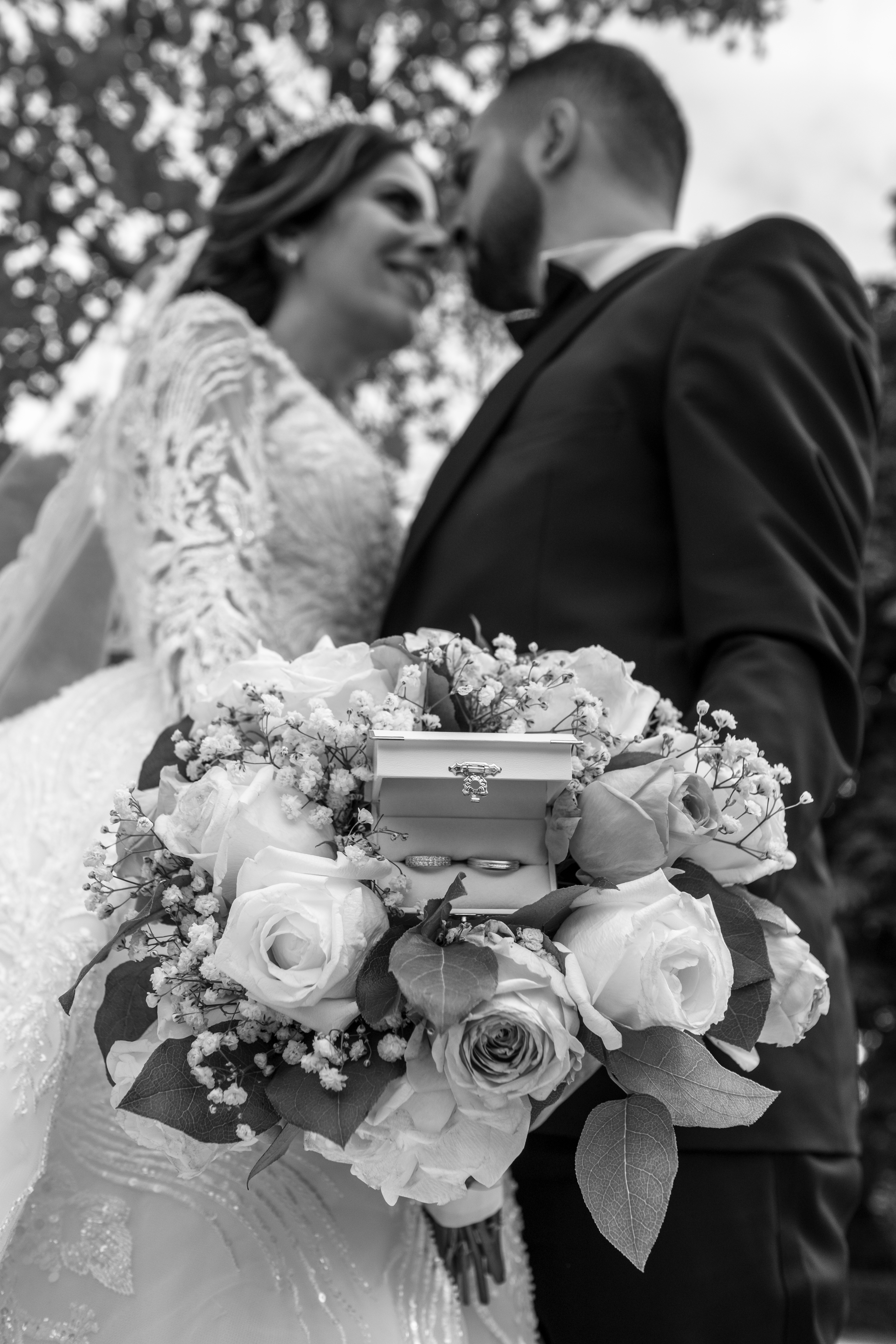 Photographie de mariage en noir et blanc d’un couple regardant tendrement leur bouquet de fleurs avec alliances, prise par Michel Rouabah, photographe professionnel à Paris, Île-de-France.