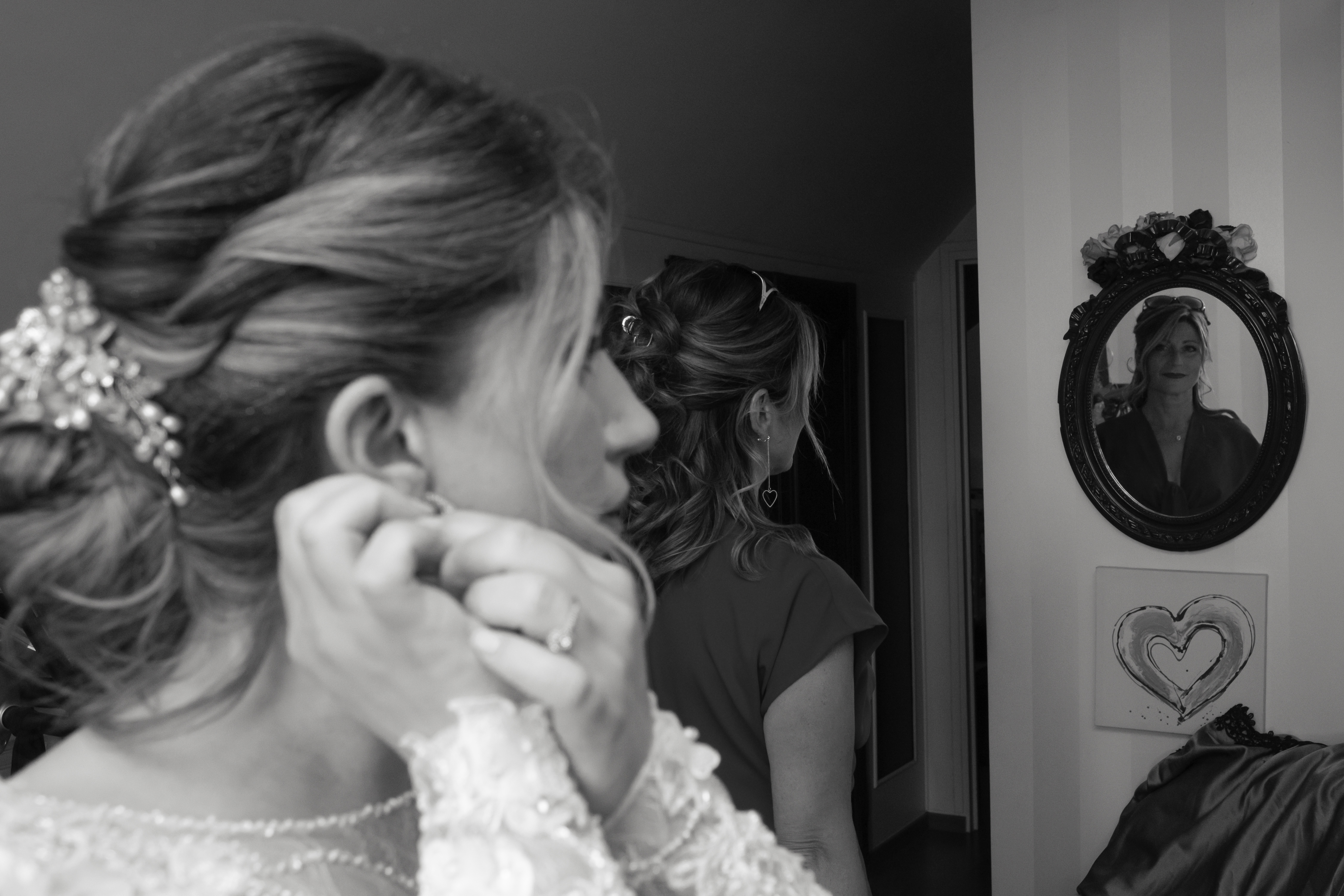 Mariée en noir et blanc ajustant ses boucles d’oreilles devant un miroir où se reflète sa mère, photo de mariage intime prise par Michel Rouabah à Paris.